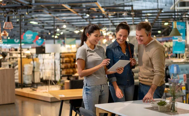 vrolijke verkoop vrouw die een ontwerp toont op tablet tot mid adult couple op zoek naar meubels in een thuiswinkel - showroom stockfoto's en -beelden